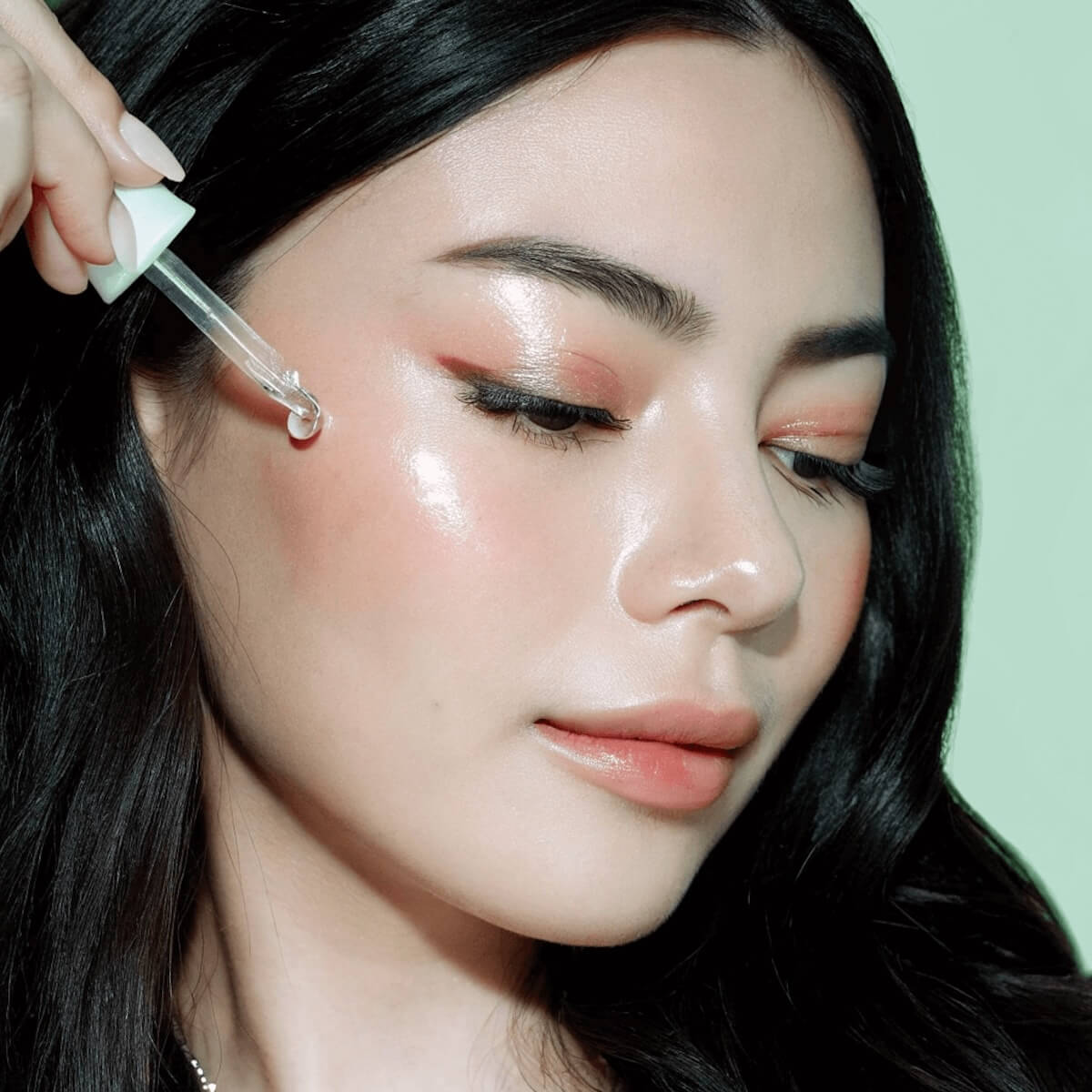Brunette with glowing skin and rosy cheeks applies a serum to her cheeks.