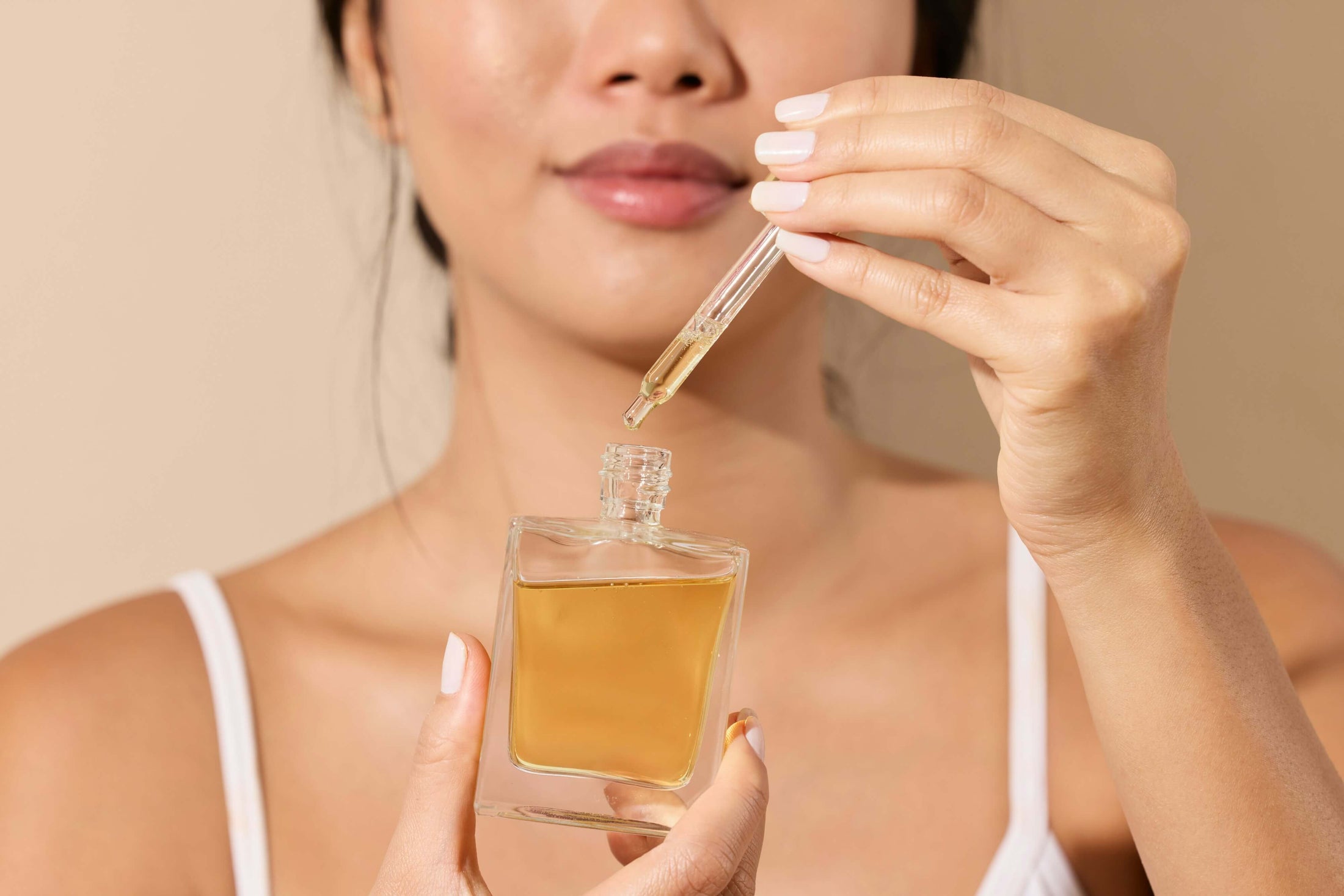 Woman holds a dropper over a bottle of essential oil.