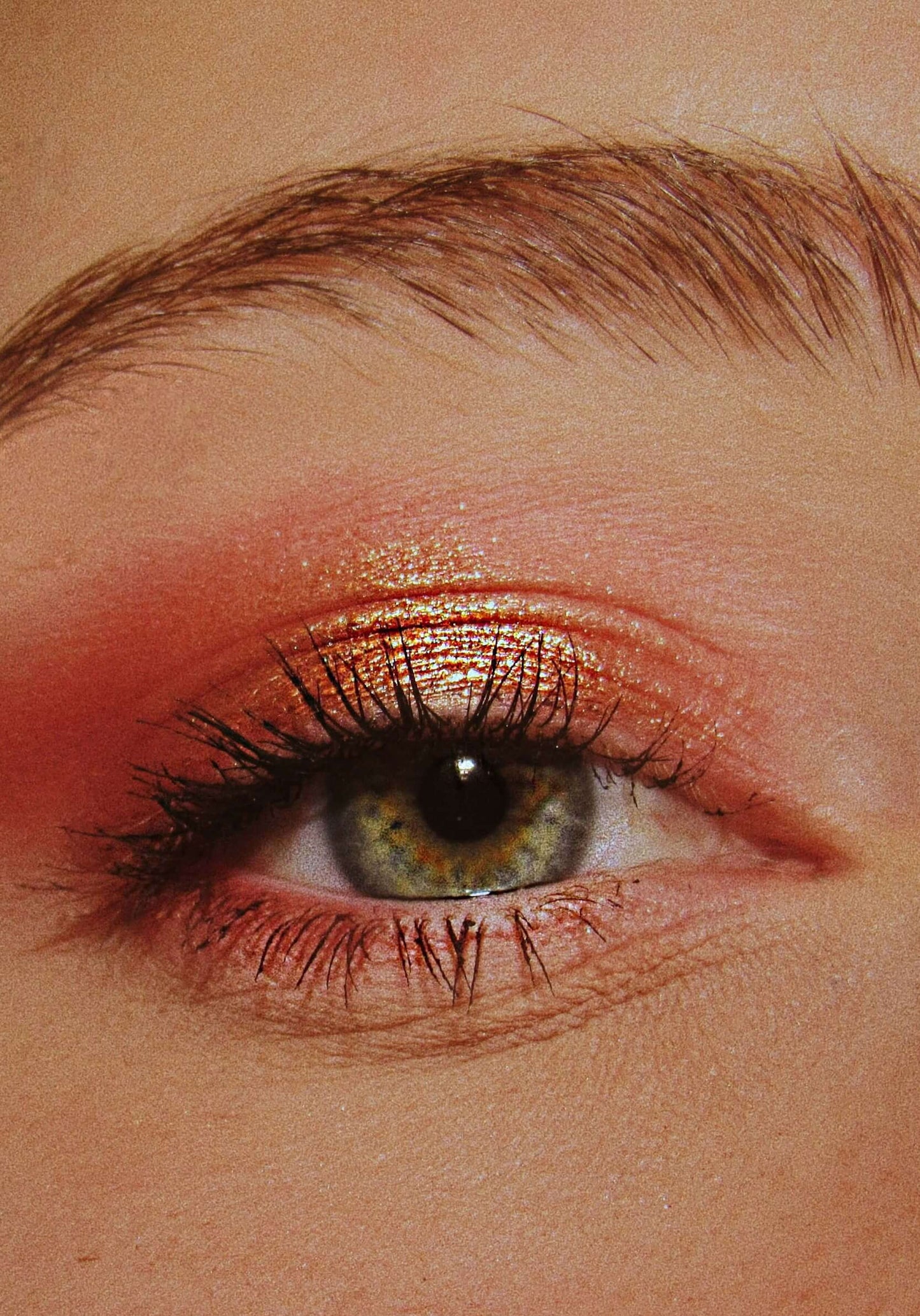 Close-up of a model's eye with pink/red metallic eyeshadow and black mascara.